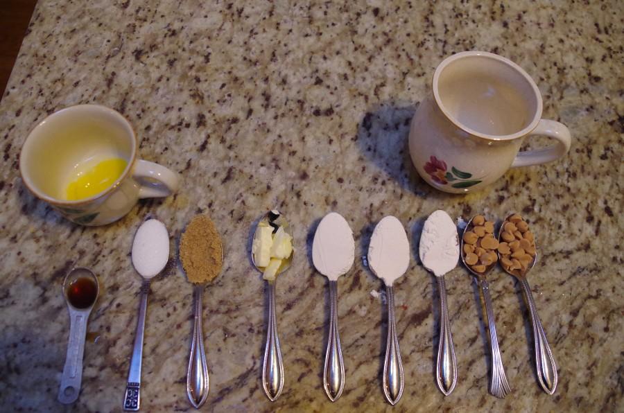 From left to right are the ingredients needed to make your cookie in a mug:  1/2 Teaspoon of Vanilla Extract, 1 egg yolk, 1 tablespoon of sugar, 1 firmly packed tablespoon of brown sugar, 1 tablespoon of butter, 3 tablespoons of flour, 1-2 tablespoons of chocolate chips (I used peanut butter chips here)