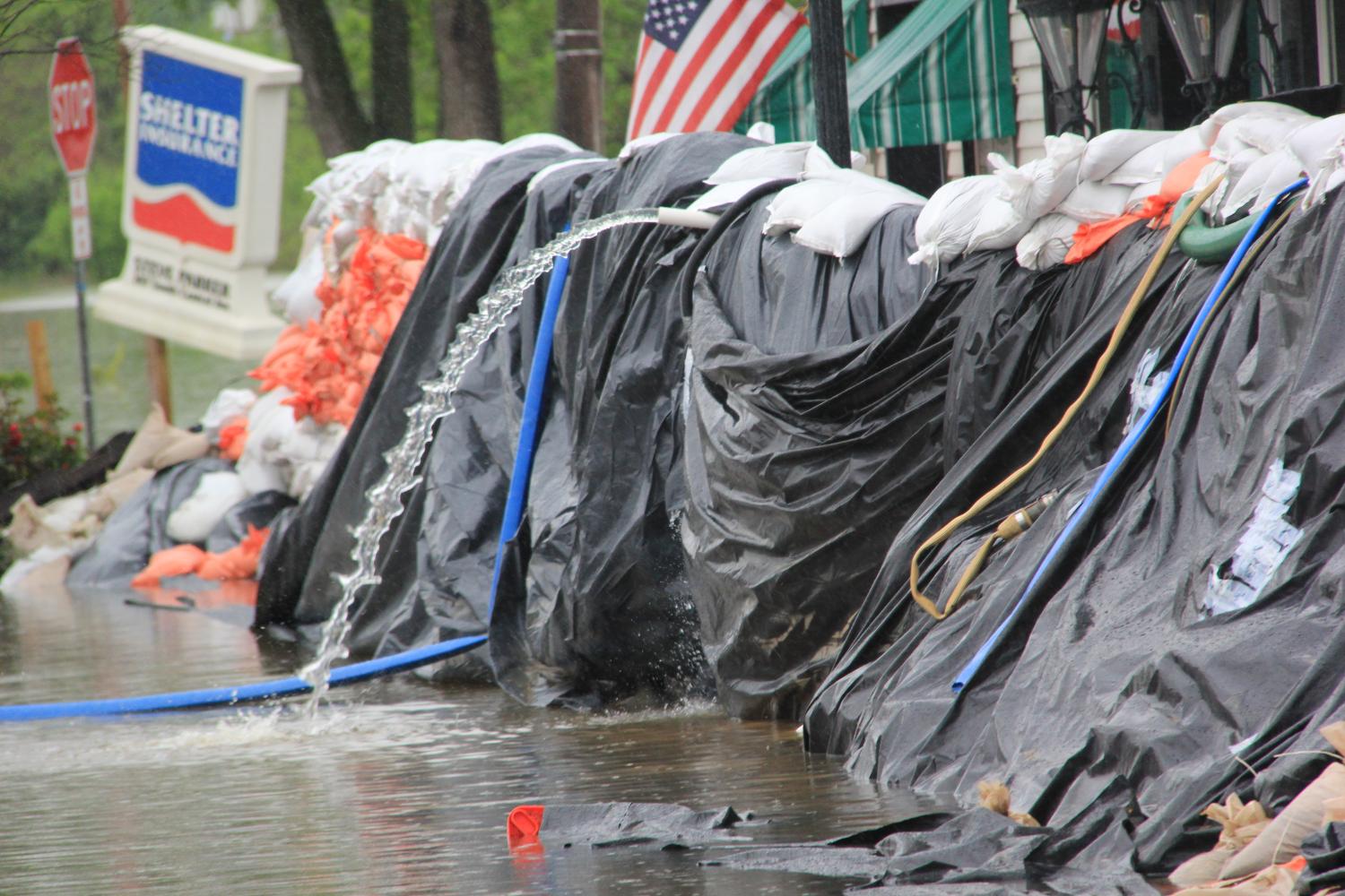 A hose is used to pump water away from stores over a wall of sandbags. This process is used to remove any water that may have made its way past the sandbags.