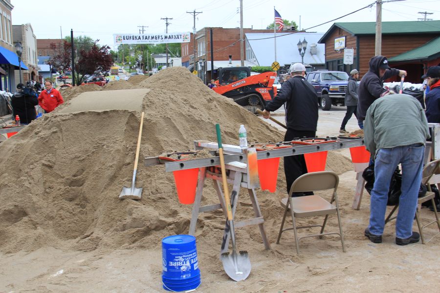Volunteers shovel sand into bags using the sandbagging contraption.