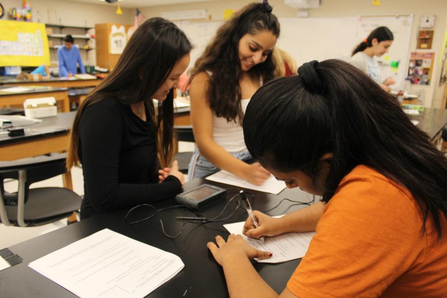 Karena Wong, senior, and Rosanne Gerami, senior, discuss their groups’ results of the friction during the lab while Aishva Kothari, junior, records the results on her lab sheet.