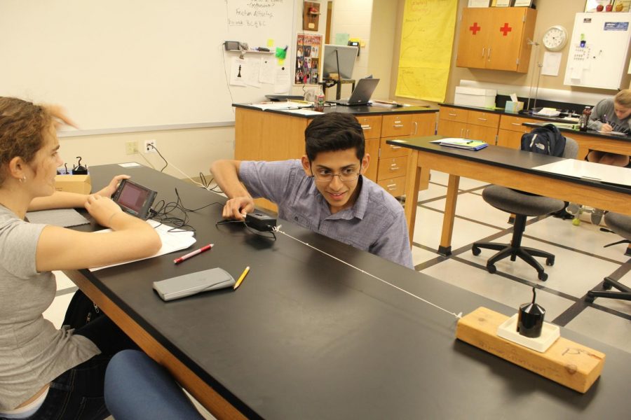 Kshitij Sinha, junior, carefully pulls the device along the table in order to accurately determine the friction in AP Physics. His group members Lalit Trivedi, junior and Ashley Skaggs, junior, point him in the right direction.
