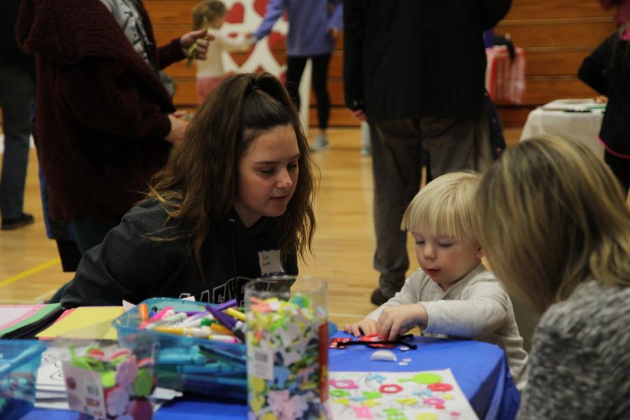 As a child creates a craft at the Winter Carnival, freshman Zoe Smith watches.