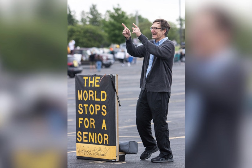 Retiree Paul Krull. math teacher, congratulates the Class of 2020 at their Farewell Parade on May 21.  He displayed his infamous The World Stops for a Senior sign.