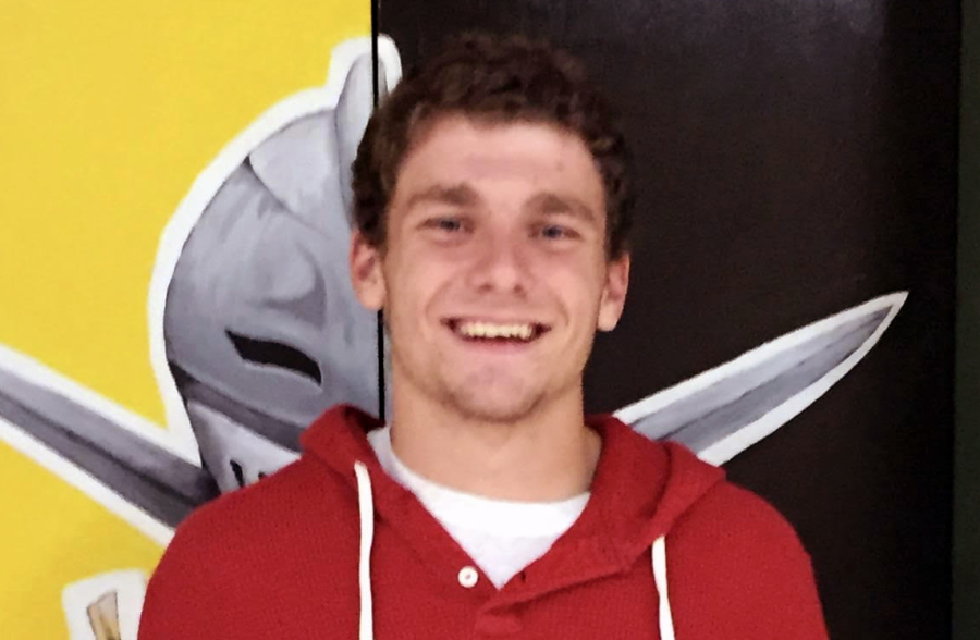 Class of 2015 graduate Matthew Waeckerle smiles in front of a Lancer logo in the Gym. Waeckerle was involved in multiple sports though his high school years and has now returned as a history teacher.