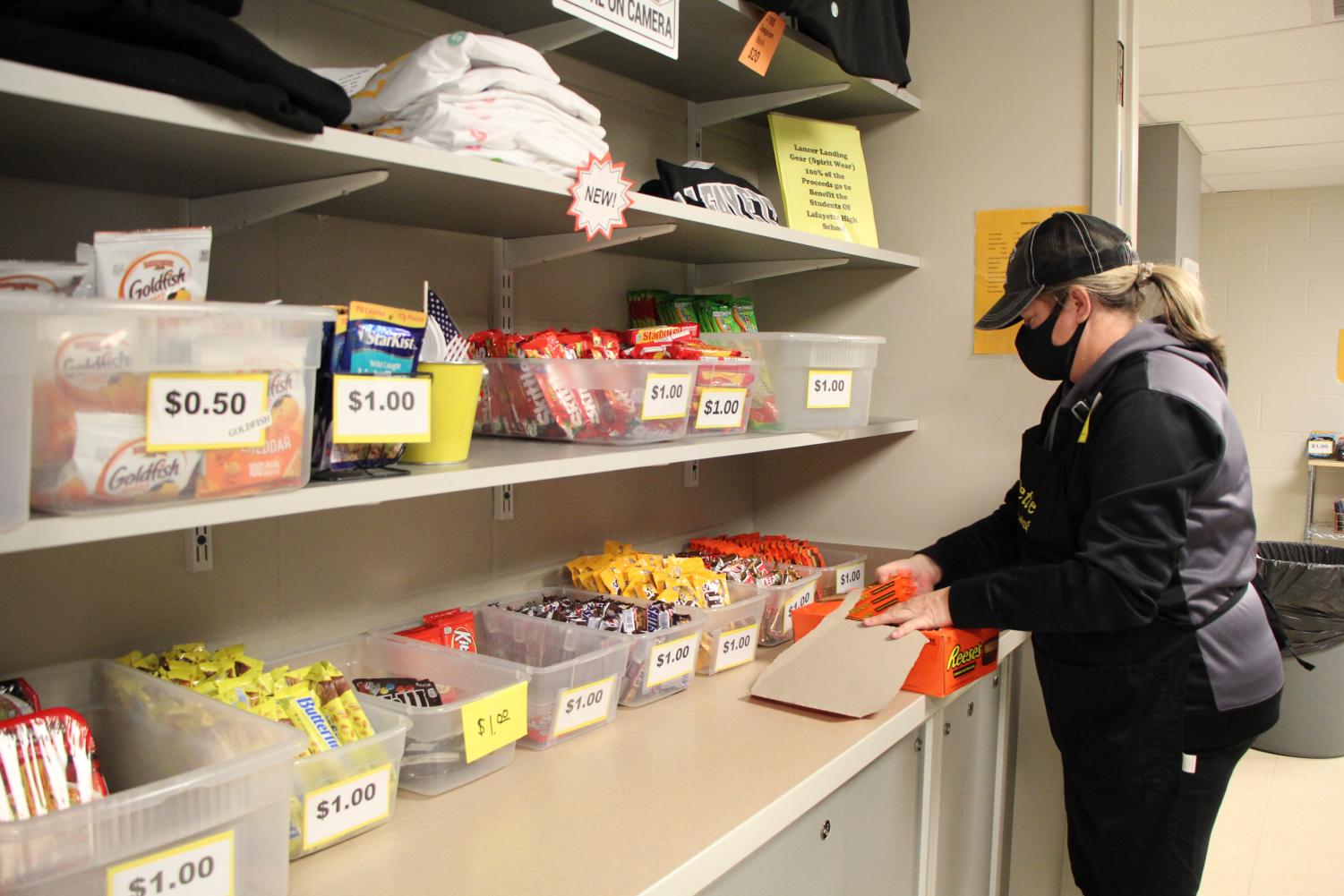 School Store manager Michelle McSpadden restocks food item on the shelves in Lancer Landing during the lunch shifts.  LPO said more volunteers are needed to keep the school store open regularly.