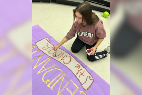 Senior and choir Homecoming chair Julia Cundy paints a banner that will go on the choirs Homecoming Parade float. Cundy has spent time after school in the choir room to prepare for the Homecoming Parade.