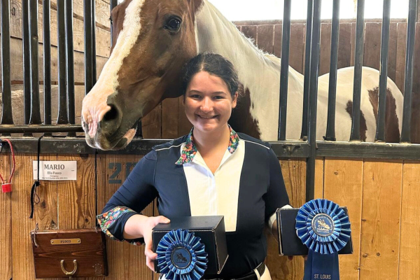 After participating in the St. Louis National Charity Horse Show, senior Ella Fusco stands next to her horse Mario with two first place ribbons.
