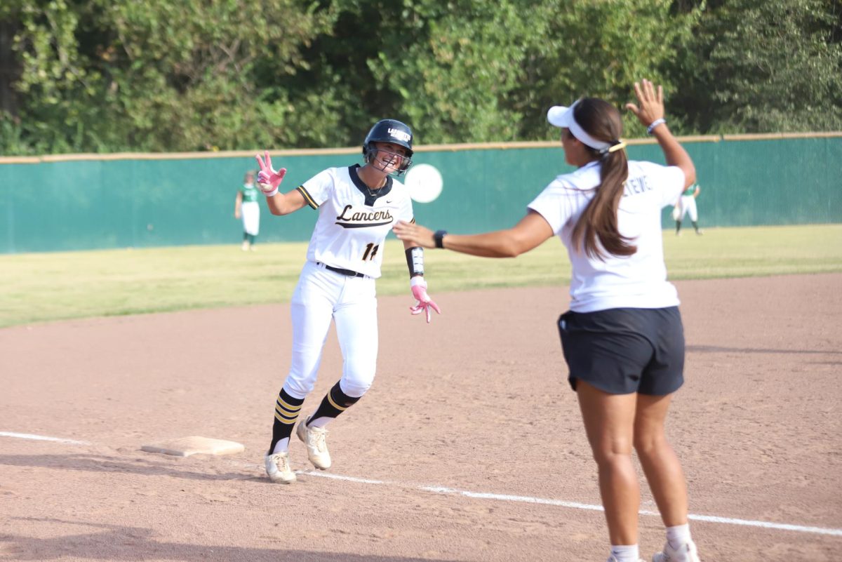 With her hand in the air, junior batter Sidney Vogt gets ready to high five her coach on a run to home-plate. Vogt hit a grand slam this game to lead the Lancers to a 16-1 blowout against St. Joe, Sept. 2.