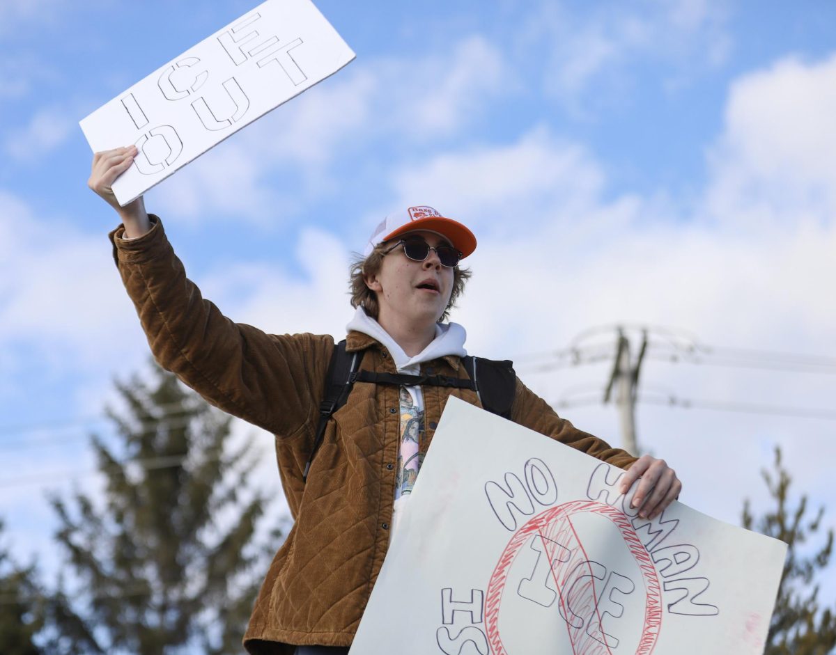 While protesting, freshman William Webb brandishes his signs on the sidewalk. Webb held two signs that read "ICE out" and "No human is illegal."