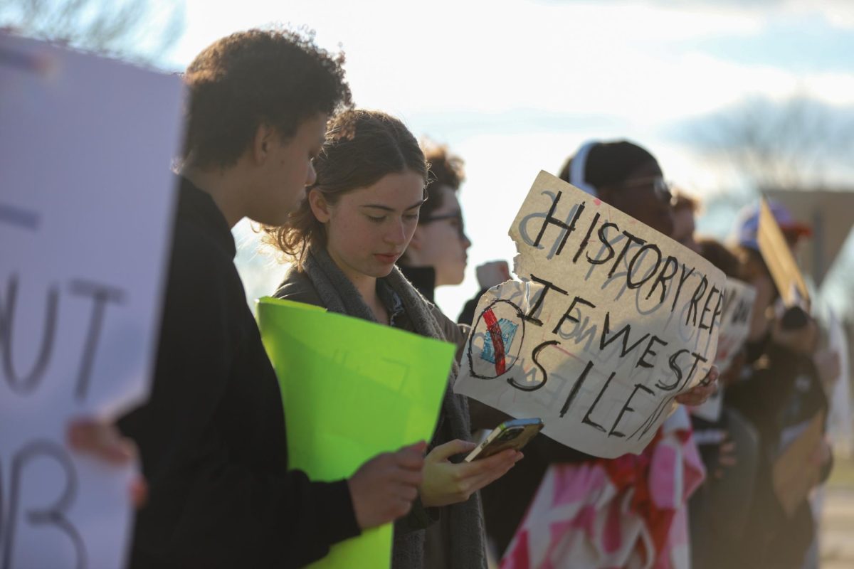 While holding a sign, sophomore Zoe Faw looks down at her phone. Faw held a sign that said "History repeats if we stay silent." "If we don't try to change the things that are happening right now, it will surely get worse," Faw said.