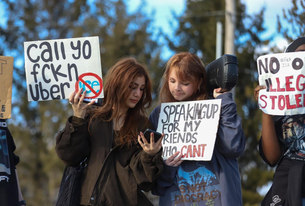 While holding signs, seniors Aiza Khan and Riley Kummer look down at Kummer's phone. Many students who participated in the walkout stayed after school to continue protesting. 