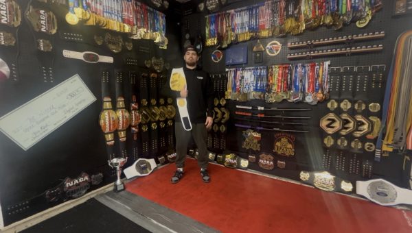 Holding a championship belt from the Double Gold Invitational, senior Mason Stritzel stands in the center of the trophy room at his house. This room contains a total 372 pieces of hardware from tournaments all over the United States.